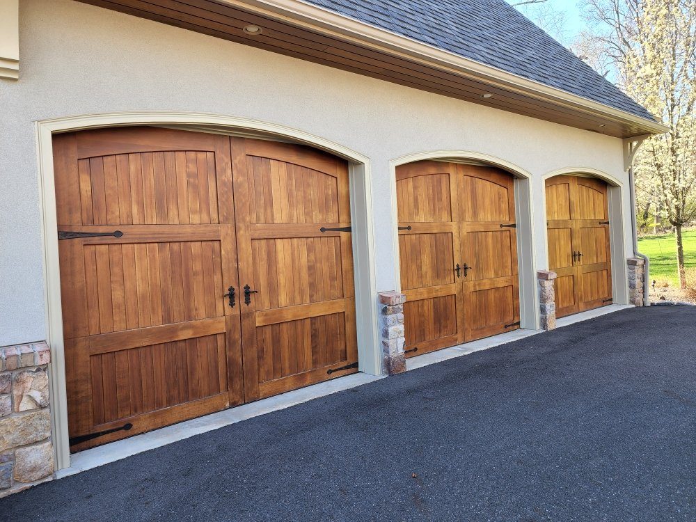 Three arched Artisan custom wood carriage garage doors with wrought-iron hardware installed on a stucco home