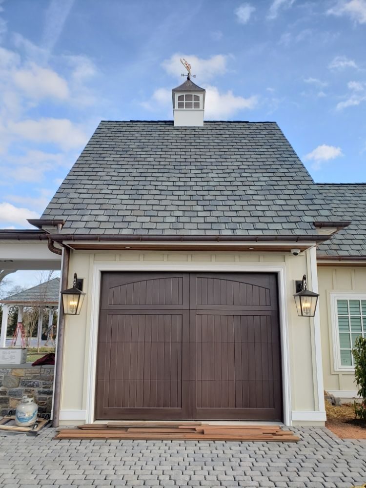 Brown carriage-style garage door on a slate-roofed carriage house with cupola and copper gutters