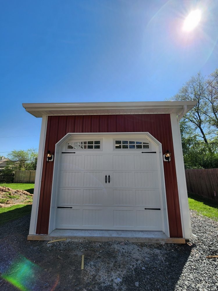 White carriage-style door with decorative hardware on a red board-and-batten garage