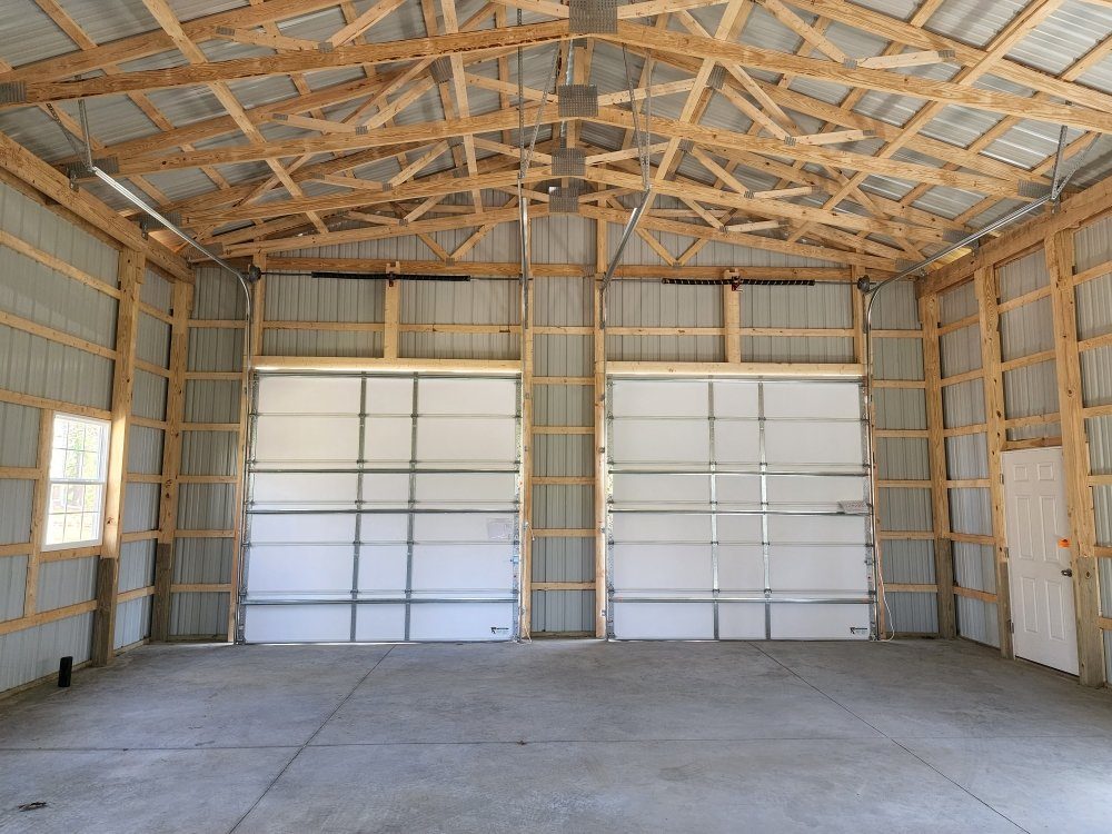 Pole barn interior showing two white sectional doors with high-lift track and torsion assemblies