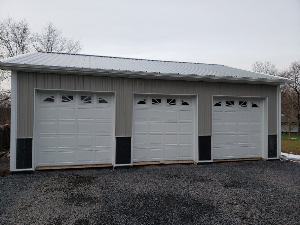 Three white raised-panel garage doors with sunburst windows on a pole barn