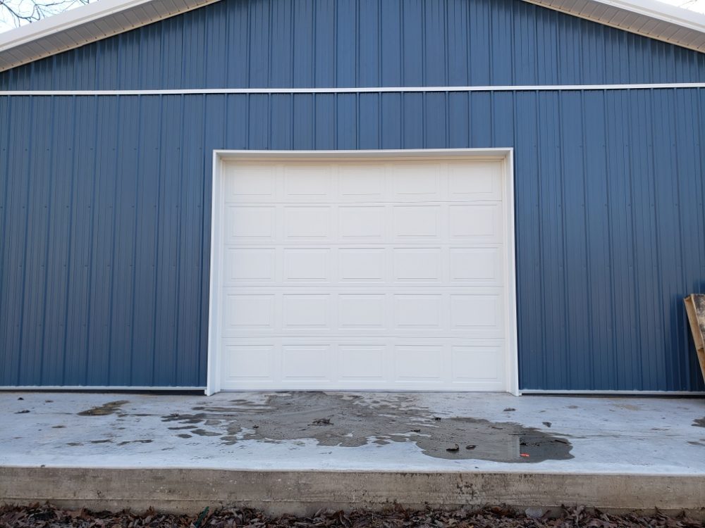 White raised-panel sectional door installed in a blue steel pole barn