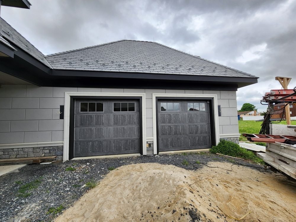 Two grey wood-grain garage doors on a new-construction home with slate roof
